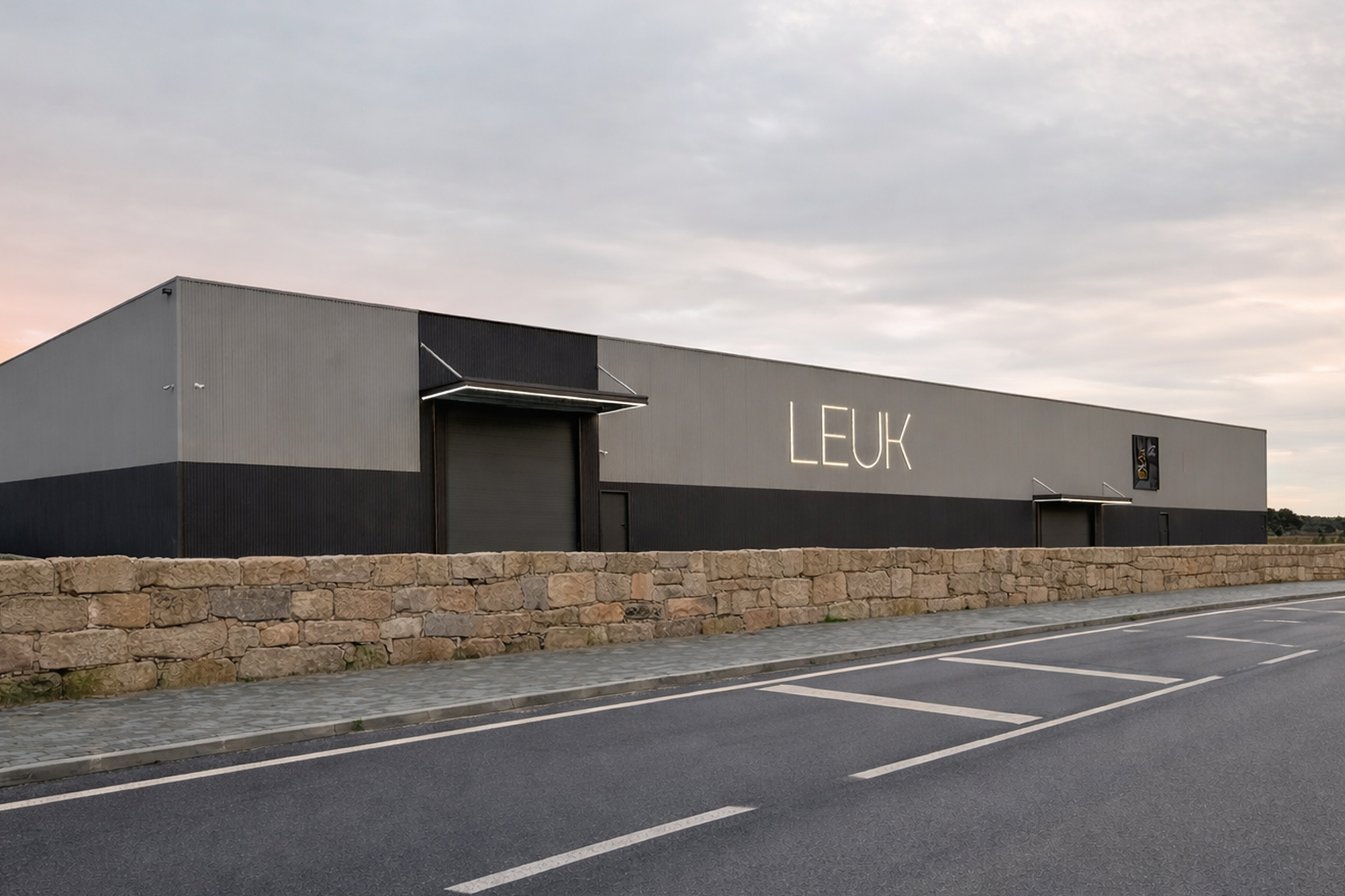 Fachada exterior do pavilhão industrial da LEUK com muro de pedra e acesso rodoviário
